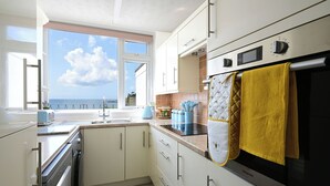 A modern kitchen with white cabinets, a built-in oven, and a view of the sea through a large window.