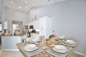 A modern kitchen with white cabinetry, granite countertops, and a dining area set for six with a granite table.