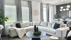 Un salon moderne avec un canapé d’angle, une table basse ronde et un coin repas agrémenté d’un mur aux motifs noir et blanc.