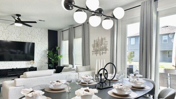 Une salle à manger moderne avec une table ronde dressée pour six personnes, un téléviseur à écran plat fixé au mur et un ventilateur de plafond.
