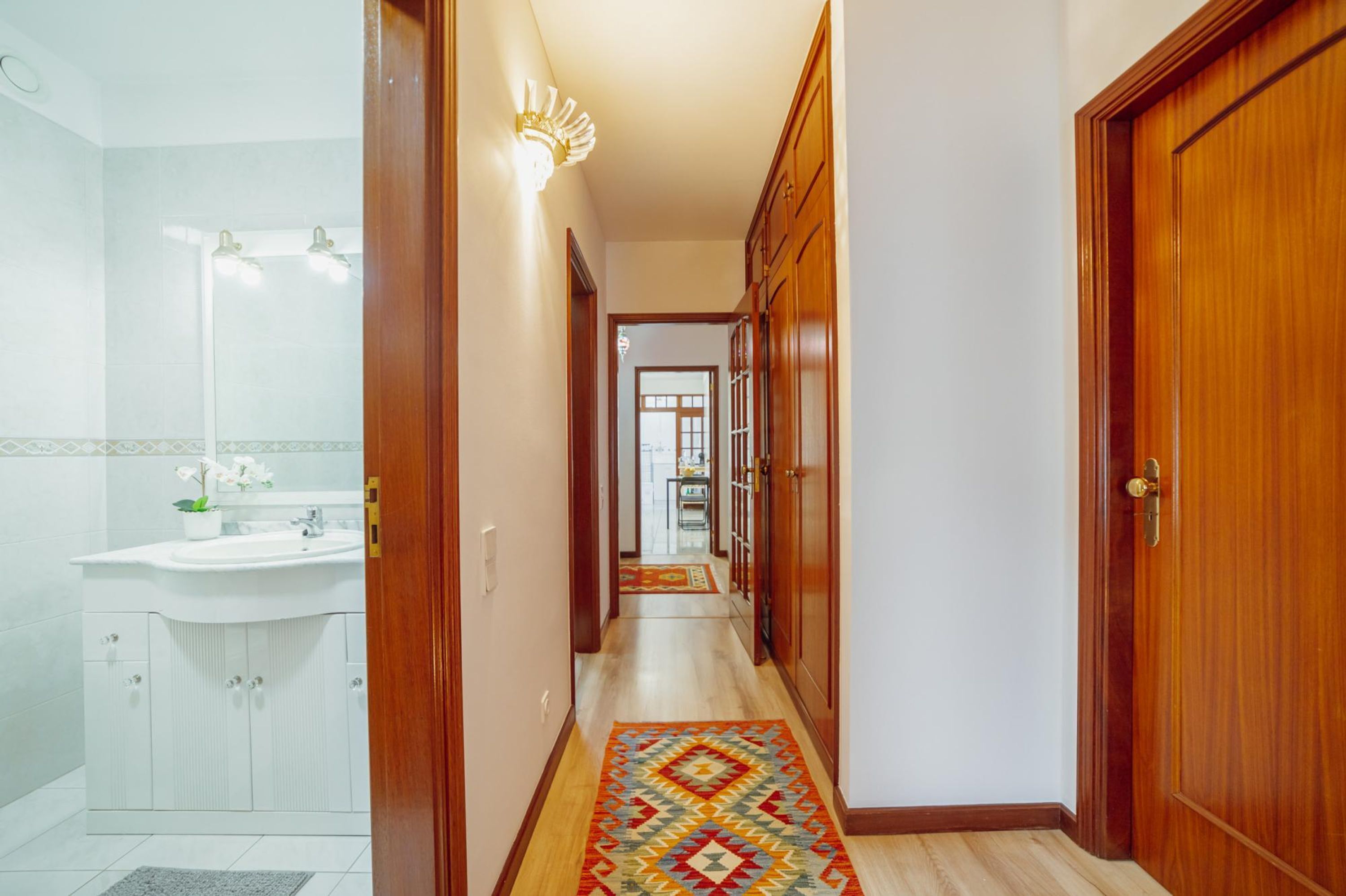 A hallway with a wooden door, a white sink, and a patterned rug.