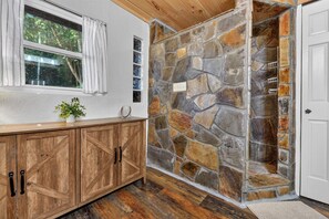 A room with a stone wall, wooden cabinets, a window with curtains, and a door.