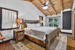 Quarto com estrutura de cama de madeira, ventilador de teto, mesa de cabeceira e vista para o exterior.