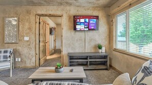 Un saló amb un televisor penjat a la paret que mostra diverses plataformes de streaming, un sofà, una taula de centre amb una planta i una banca.