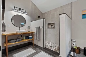 A modern bathroom with a wooden vanity, a round mirror, a shower with a hexagonal tile pattern, and a towel rack.