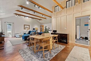 A spacious living area with a dining table, wooden chairs, a sofa, and a bookshelf.