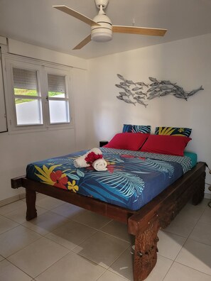Une chambre à coucher avec un lit, un ventilateur de plafond, une fenêtre et un élément décoratif mural.