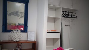 Une chambre d’hôtel comprenant un lit, un bureau, un miroir, une armoire et une étagère avec des objets décoratifs.