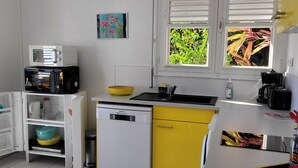 Une cuisine compacte avec des meubles blancs et jaunes, un four à micro-ondes, un évier et une fenêtre donnant sur un espace verdoyant.