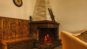 Ein gemütliches Zimmer mit Kamin aus Backsteinen, einer hölzernen Bank und einem gepolsterten Sessel.