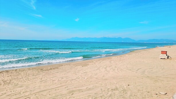 Ein Strand mit blauem Himmel, ruhiger See und fernen Bergen.