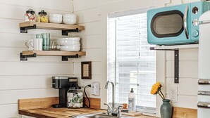 Une cuisine avec des étagères en bois, une machine à café, un évier et un micro-ondes de couleur turquoise.