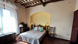 A bedroom with a bed, bedside lamps, a chair, a wooden headboard, and a window with curtains. - Mas Tapet, Masia Ideal per Família, Amics o Grups (Vilanova i la Geltrú)