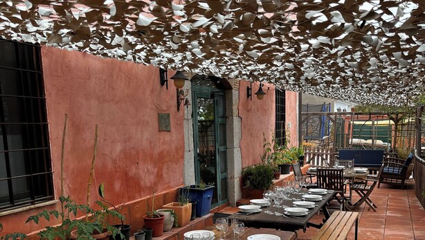 A covered outdoor dining area with wooden tables and benches, potted plants, and a stone wall. - Mas Tapet, Masia Ideal per Família, Amics o Grups (Vilanova i la Geltrú)