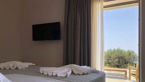 A hotel room with a bed, a flat-screen TV on the wall, and a view of the outdoors through a large window.