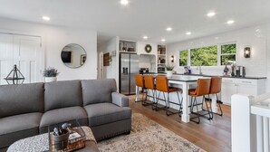 Eine moderne Küche mit weißen Schränken, einer Essecke mit Barhocker und einem grauen Sofa.