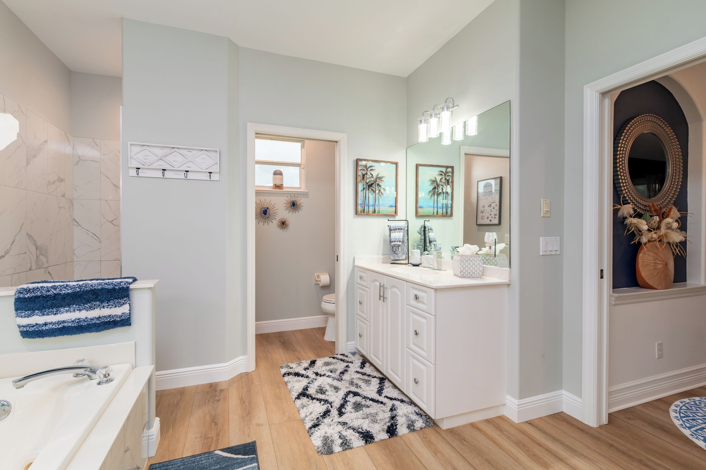 A modern bathroom with a white vanity, a blue towel, a patterned rug, and a mirror with decorative lights.