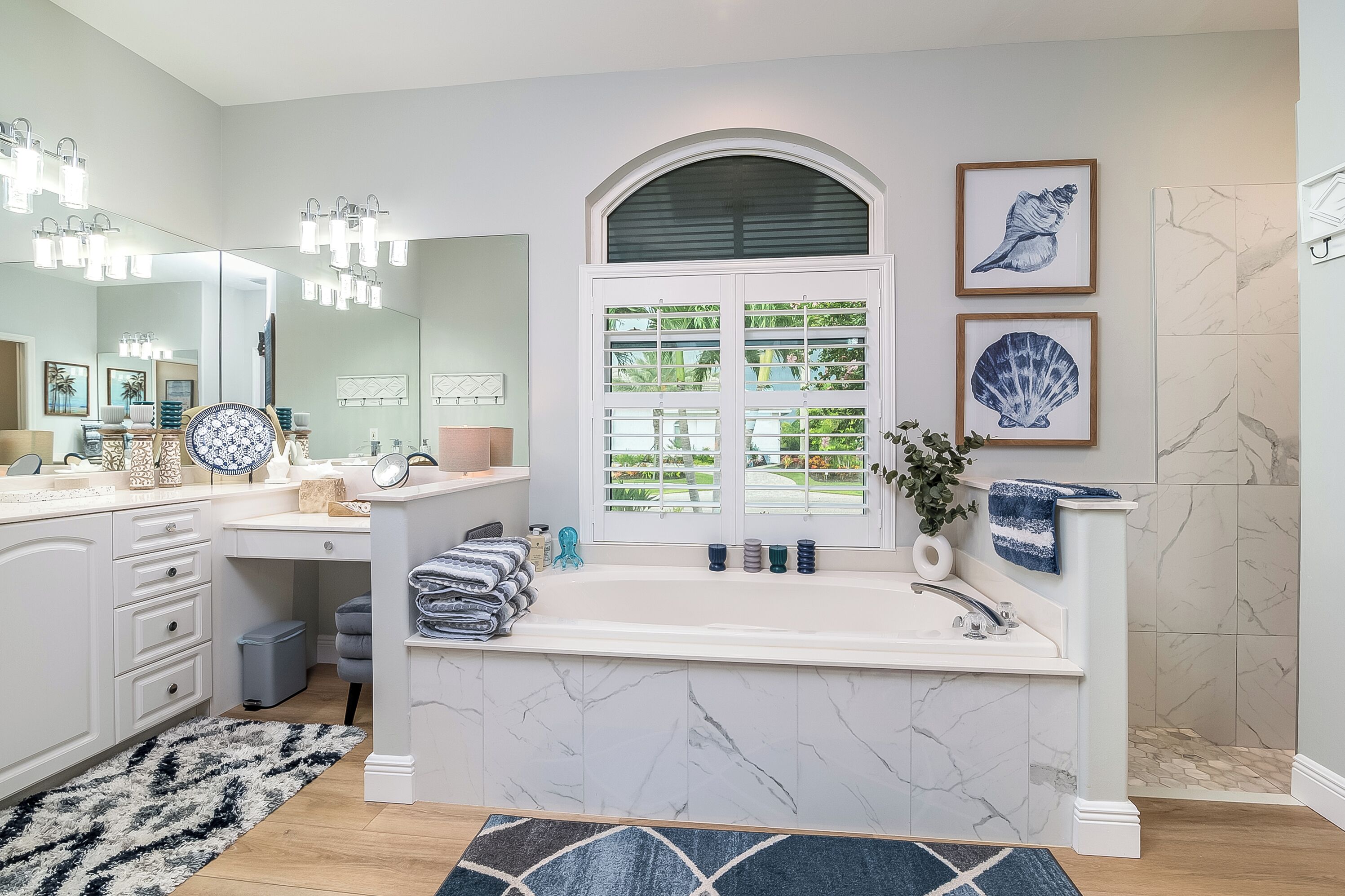 Une salle de bain moderne avec un grand miroir, un meuble-lavabo, une baignoire et une fenêtre donnant sur un paysage verdoyant.