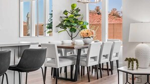 A modern kitchen with white cabinetry, a dining area with white chairs, a large plant, and a view of a desert landscape. - Red Rock Retreat 5 Bedroom Home (Washington)