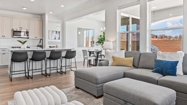 A modern living space with a grey sectional sofa, a dining area, and a kitchen with white cabinetry. - Red Rock Retreat 5 Bedroom Home (Washington)