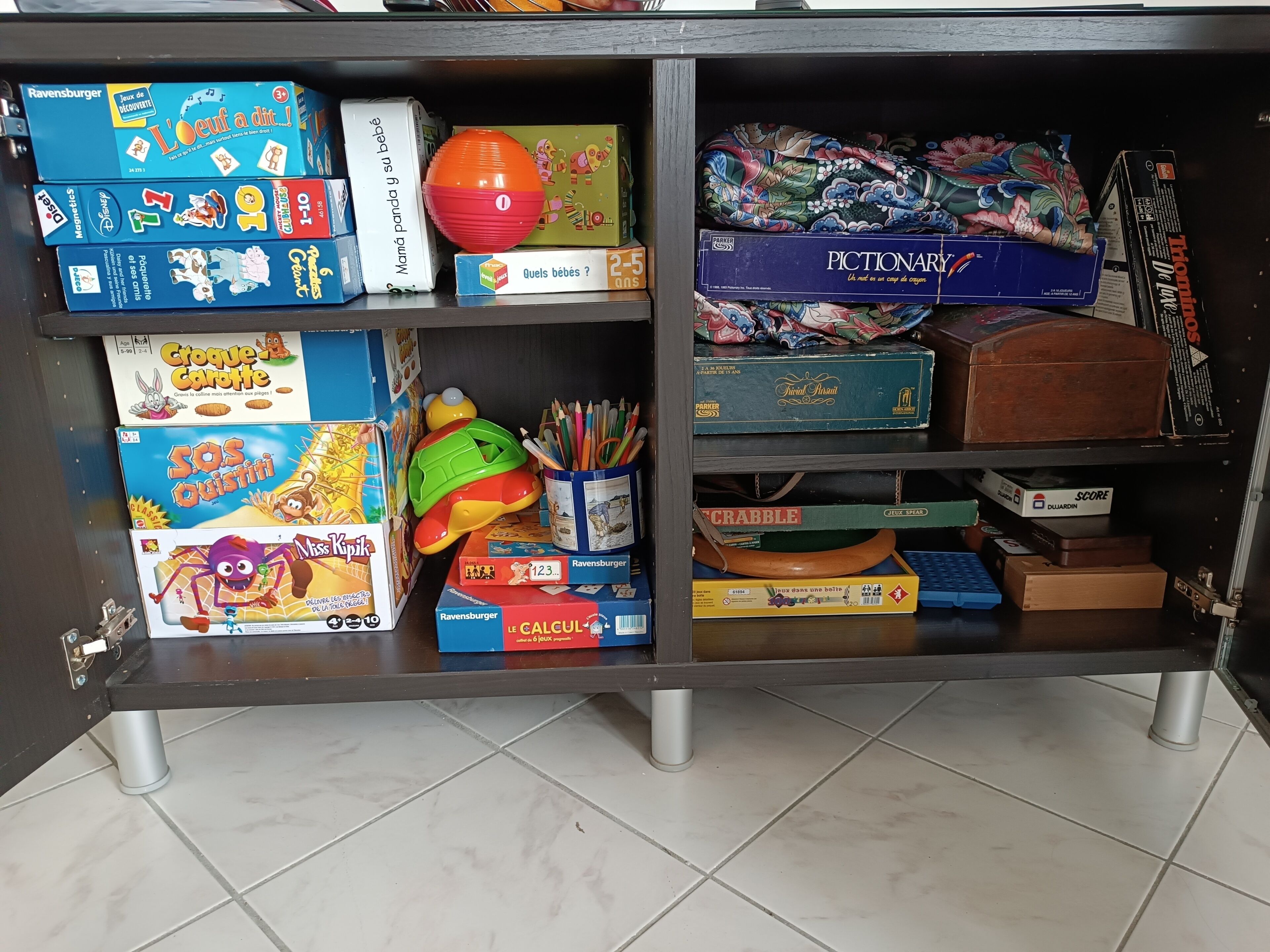 Ein Regal mit verschiedenen Kinderspielen und Spielzeug, darunter ein Zauberwürfel, ein Spielzeugauto und ein Scrabble-Spiel.