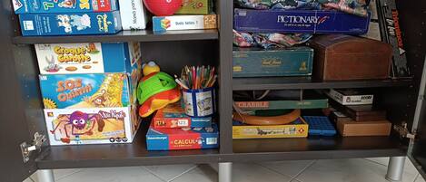 Ein Regal mit verschiedenen Kinderspielen und Spielzeug, darunter ein Zauberwürfel, ein Spielzeugauto und ein Scrabble-Spiel.