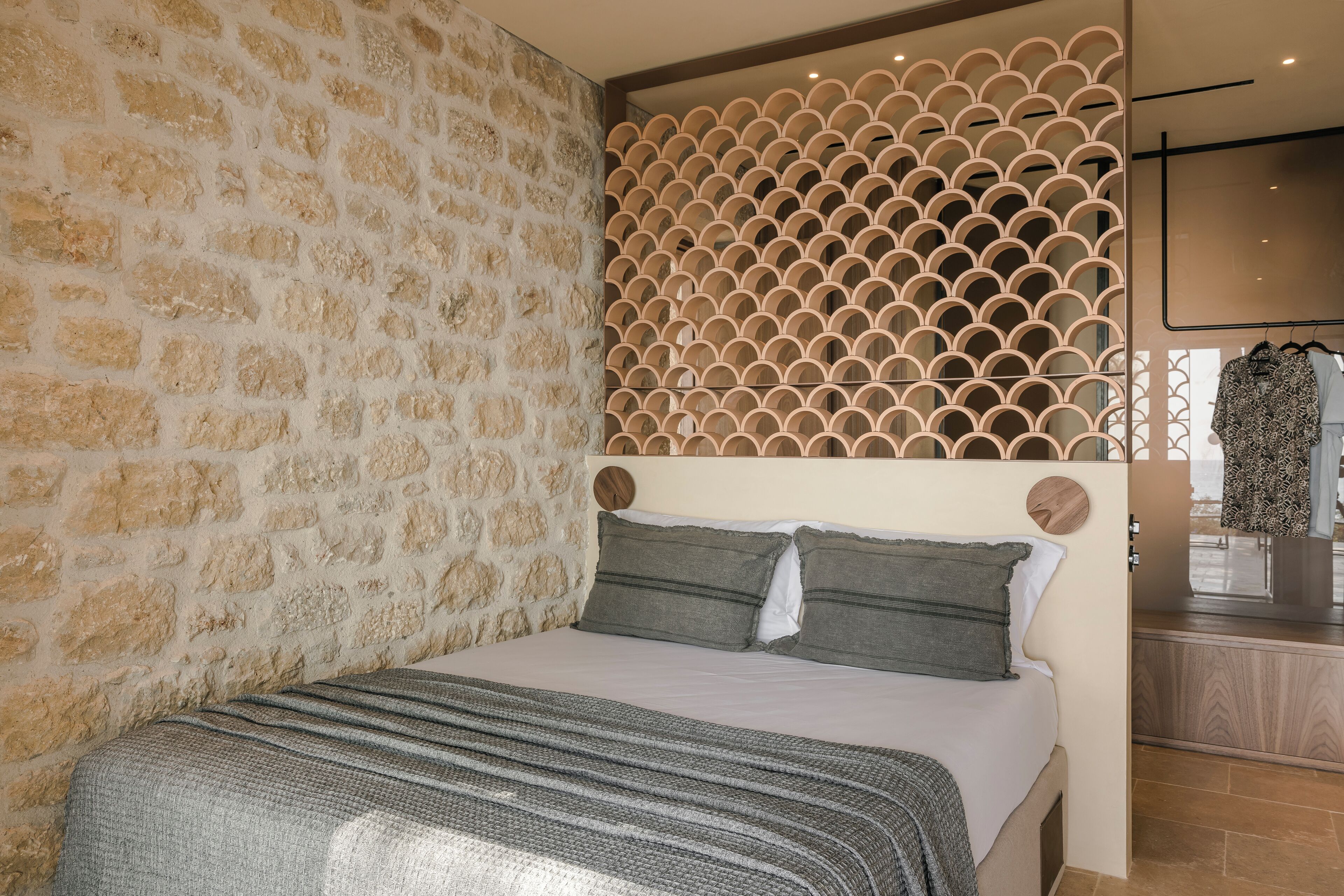 A bedroom with a stone wall, a bed with grey bedding, and a decorative wooden panel.