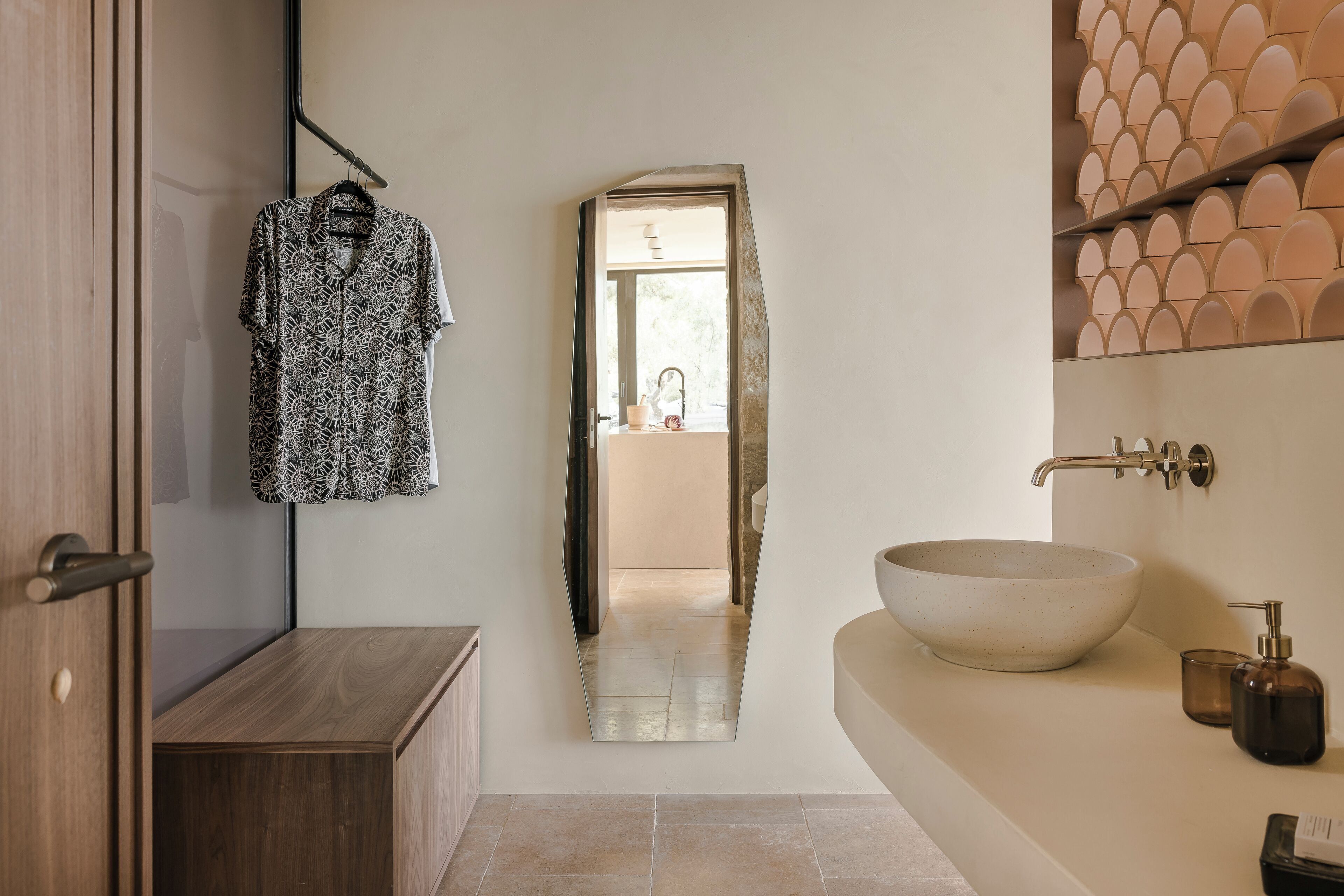 Une salle de bain avec un meuble en bois, un porte-vêtement suspendu, un grand miroir, un lavabo avec un receveur et un sol carrelé.
