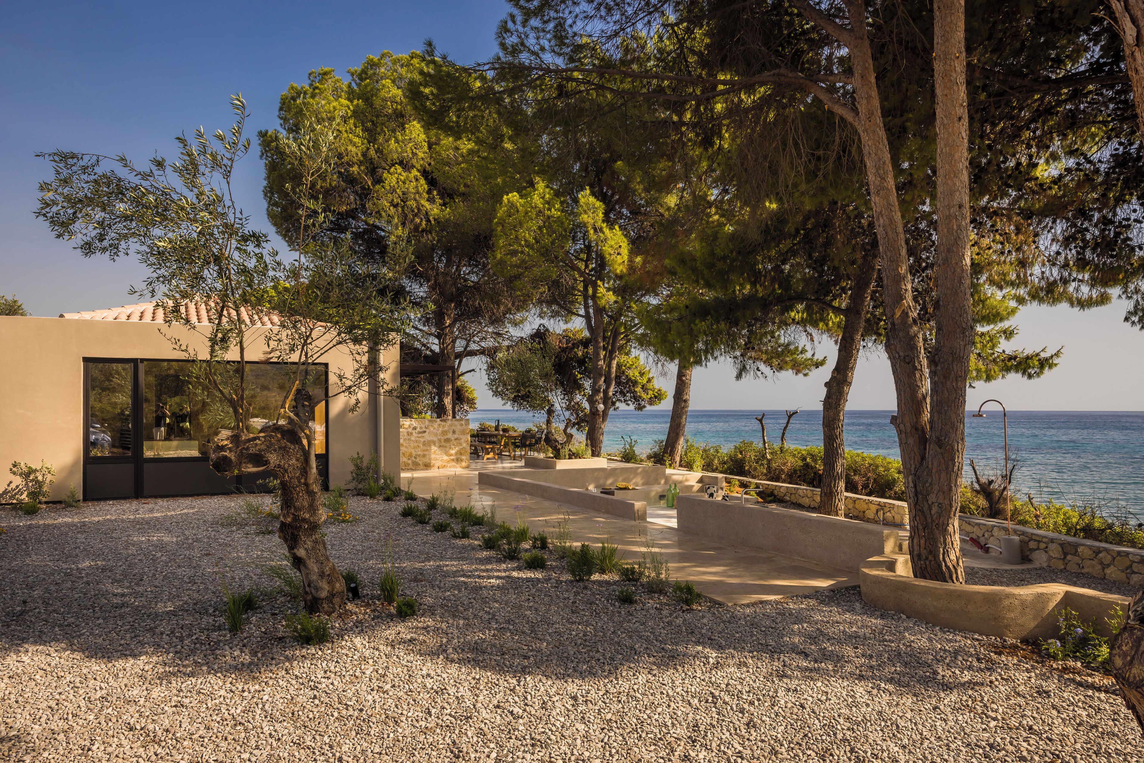 A modern outdoor patio area with a seating arrangement, a stone wall, and a view of the sea.