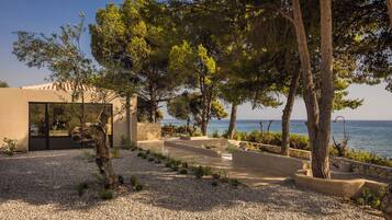 A modern outdoor patio area with a seating arrangement, a stone wall, and a view of the sea.