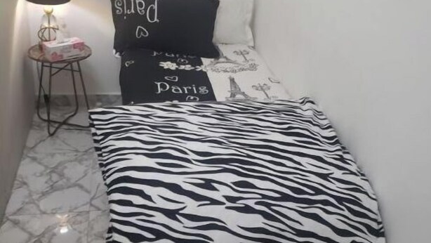 Et soveværelse med en seng, et dyreprintet tæppe, en lampe og et lille bord med en æske.