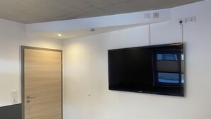 A room with a wooden door, a green bed, and a mounted flat-screen TV on the wall.