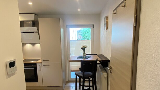 A compact kitchen with white cabinets, a built-in oven, and a dining area with a table and chairs.
