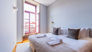 Ein Schlafzimmer mit zwei Betten, einem Fenster mit rotem Rahmen und Blick auf Gebäude.