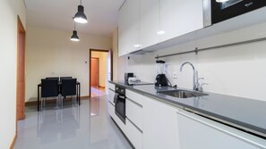 A modern kitchen with a stainless steel sink, a built-in oven, and a coffee maker. There is a dining area with two chairs and a table.