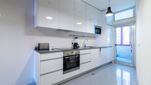 Une cuisine moderne avec des meubles blancs, un four encastré, une machine à café et un grille-pain.