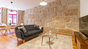 Ein Wohnzimmer mit Steinwand, einer schwarzen Couch, einem Glastisch und Holzboden.