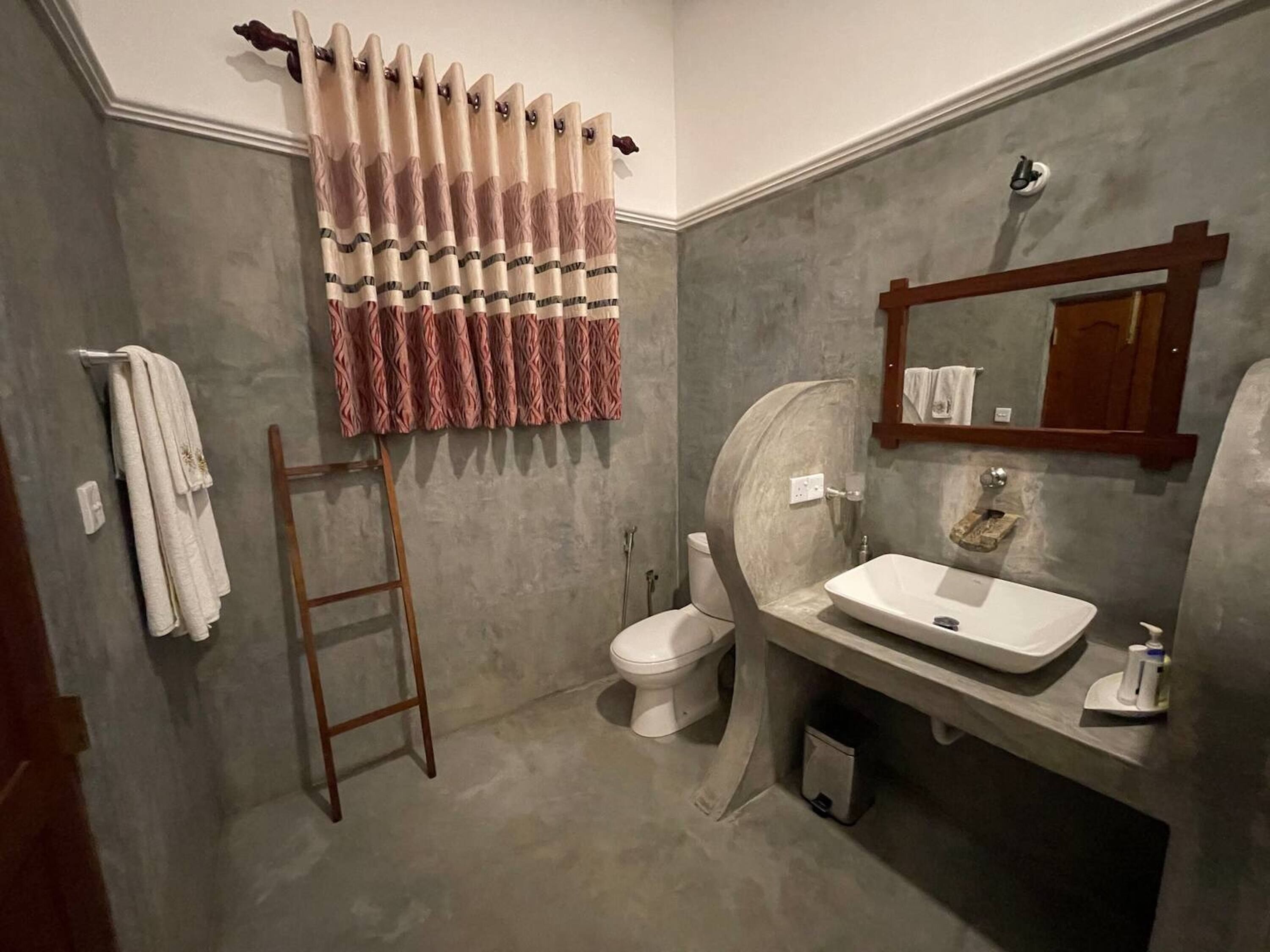 A bathroom with a wooden ladder, a toilet, a sink with a mirror, and a towel rack.
