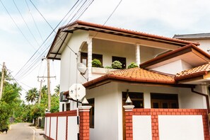 A two-story house with a balcony, a tiled roof, and a brick wall. - Younger Villa (Ahangama)