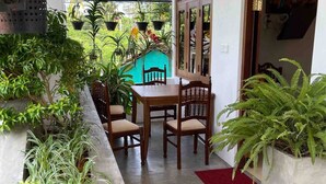 A covered outdoor area with a table and chairs, surrounded by potted plants and a decorative wooden door. - Younger Villa (Ahangama)