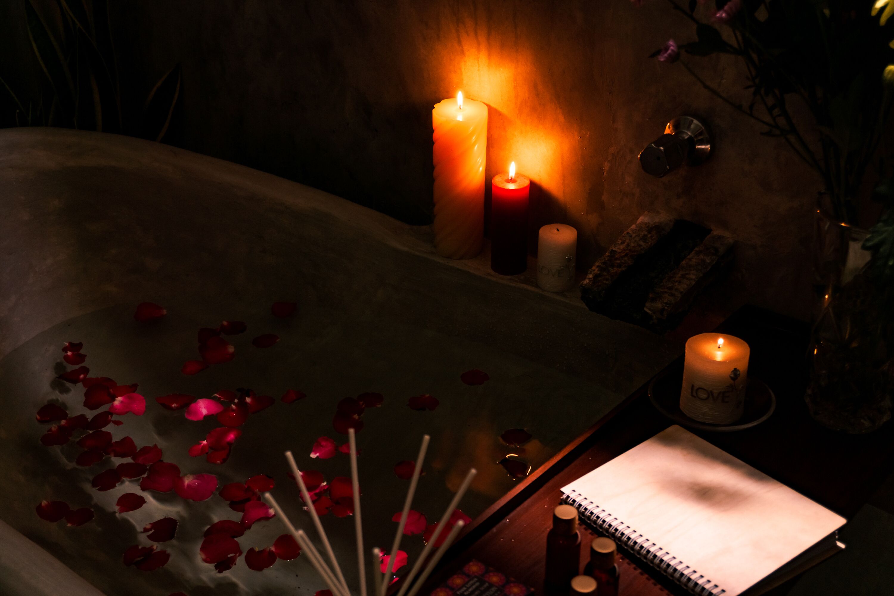 Une baignoire remplie de pétales de rose, avec des bougies et un carnet.