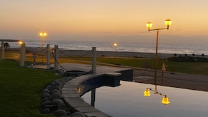 Una piscina con bordo curvo, un vialetto e vista sull'oceano al tramonto.