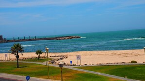 Vista sulla costa con spiaggia sabbiosa, molo roccioso e cielo azzurro limpido.