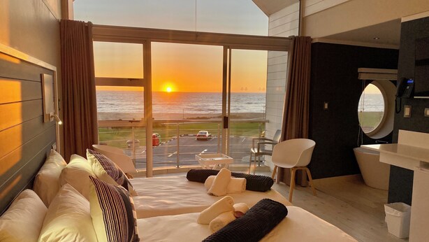 Camera d'albergo con un letto grande, una scrivania, una sedia e vista sul tramonto sull'oceano.