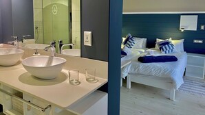 Un bagno moderno con due lavandini, uno specchio grande e una doccia. La stanza dispone di un letto con biancheria da letto bianca e numerosi cuscini.