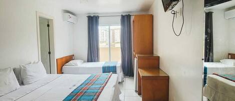 Habitación de hotel con dos camas, ventilador de techo, televisor de pantalla plana y un ventanal con cortinas.