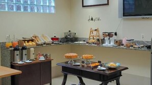 Une cuisine moderne dotée d’un bar pour prendre le petit-déjeuner, d’une grande fenêtre avec stores, d’un téléviseur à écran plat fixé au mur et d’une variété d’aliments pour le petit-déjeuner disposés sur le comptoir.