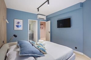 A bedroom with a bed, pillows, a TV, and an air conditioning unit.