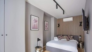 Un dormitorio moderno con una cama grande, una mesita de noche pequeña, un televisor montado en la pared y una lámpara en el techo.