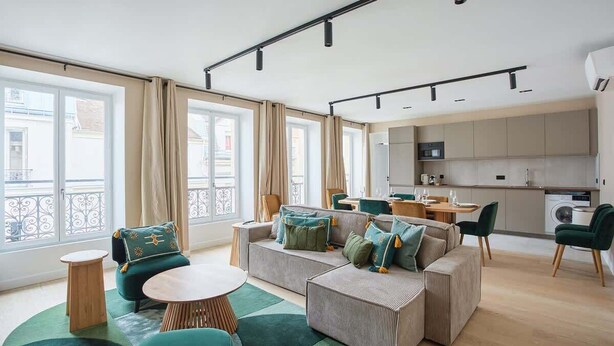 Una sala moderna con un conjunto de sofá, una mesa de centro y un comedor con sillas. Hay una cocina con armarios y electrodomésticos.